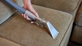 A person using an upholstery tool on the arm of a couch.