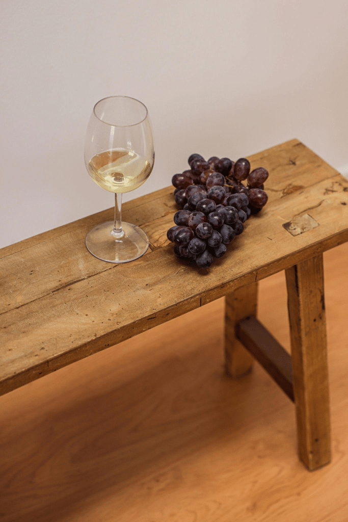 Glass of wine and grapes on a wooden bench with light-colored LVP flooring.