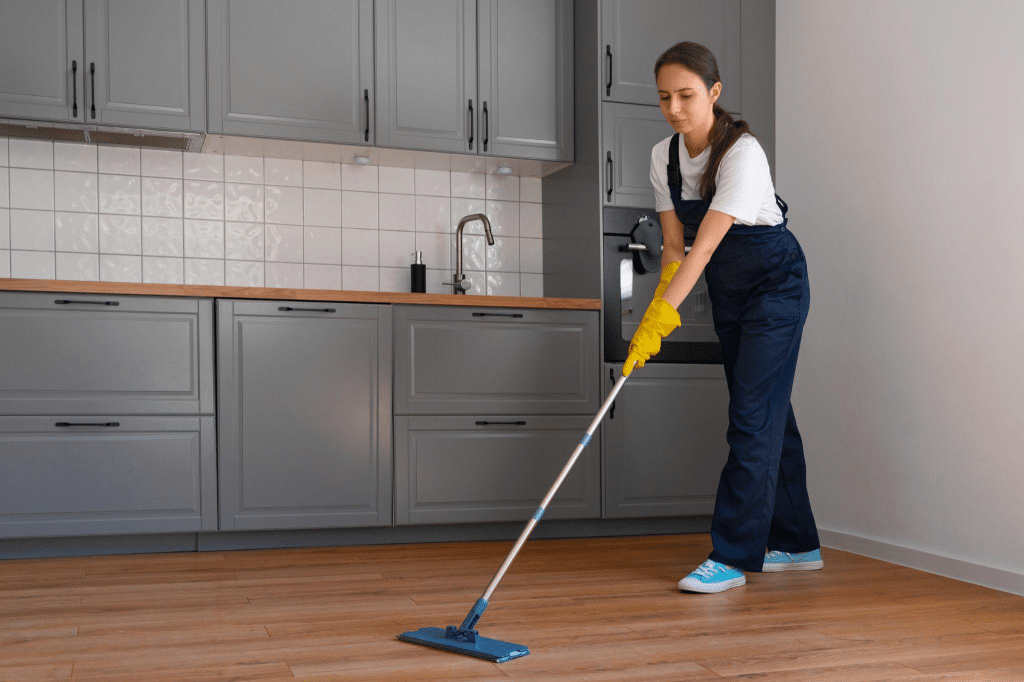 Woman wearing yellow gloves and blue overalls cleaning LVP floor