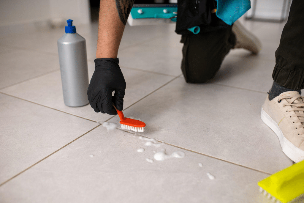 A person cleaning dirty grout with cleaning tools.