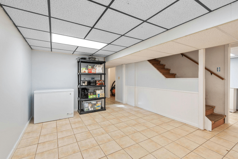 A basement with tile flooring, white walls, and a staircase.